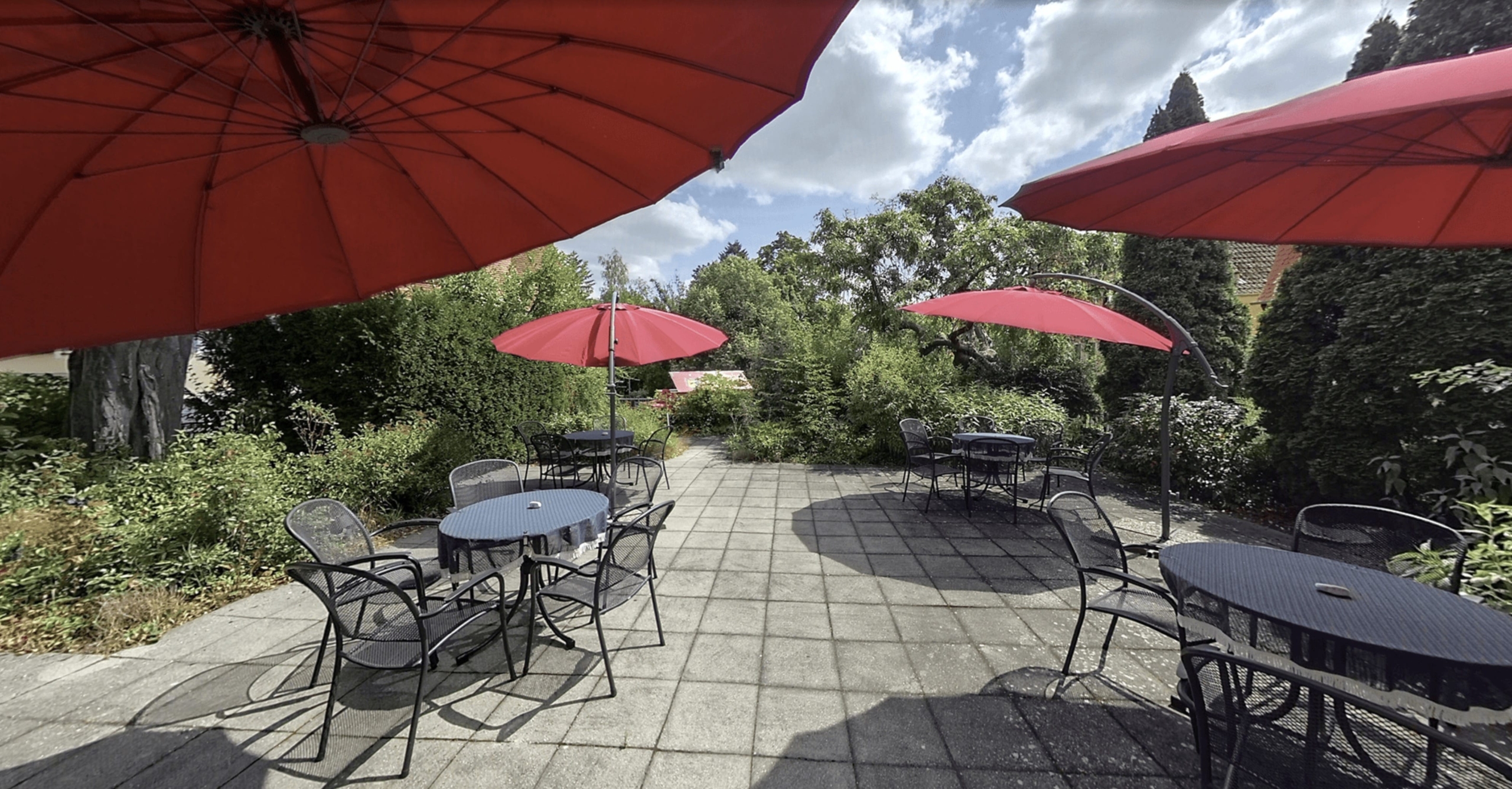 Terrasse des Café Lindenhof mit Gartentischen und -stühlen mit Sonnenschirmen