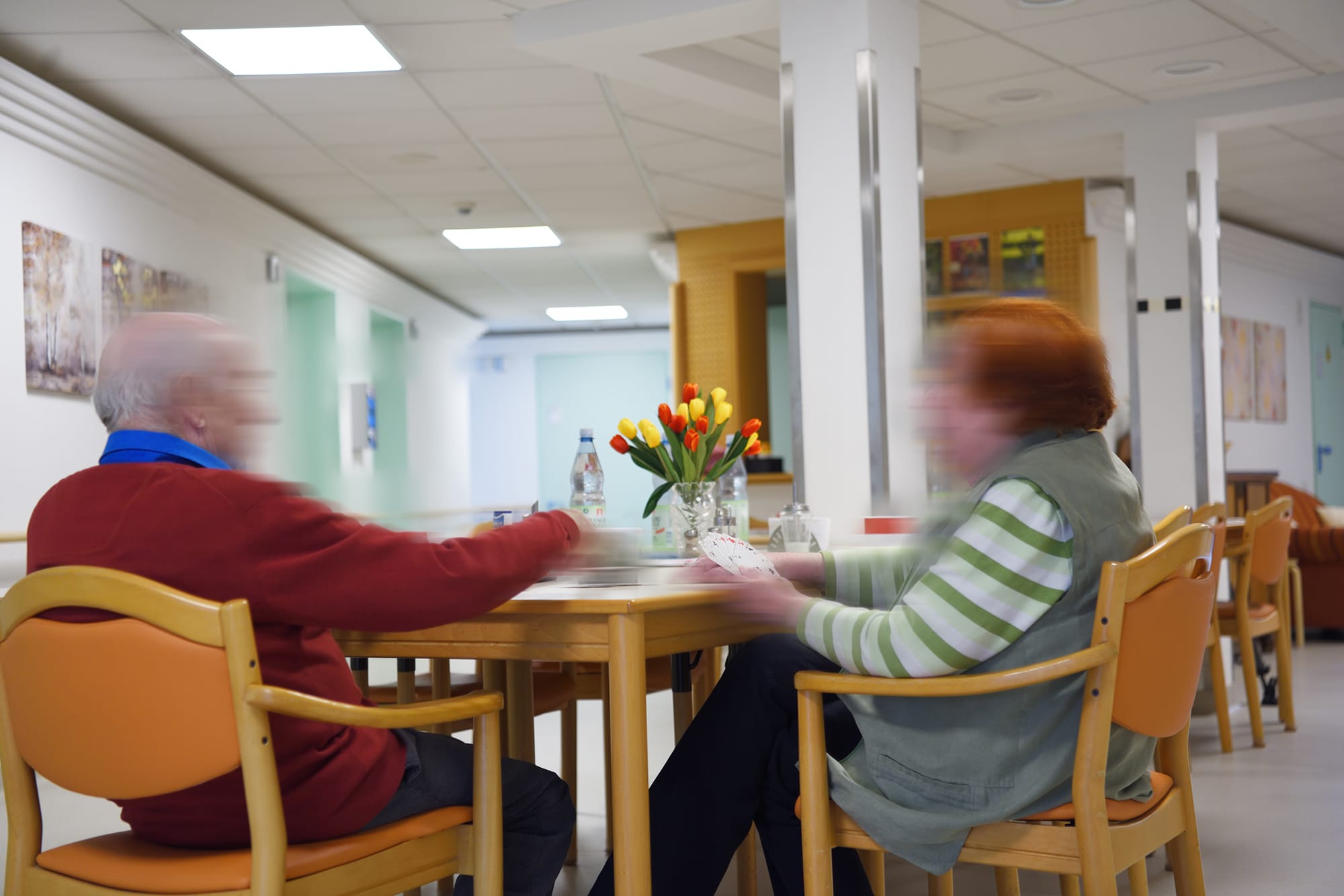 Zwei Bewohner/innen beim Kartenspielen in einer Sitzecke